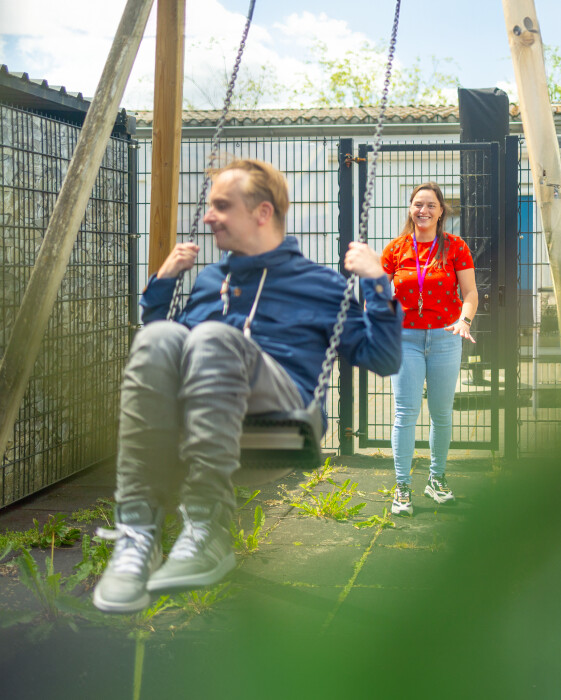 Een begeleider gehandicaptenzorg die lacht naar een cliënt op een schommel